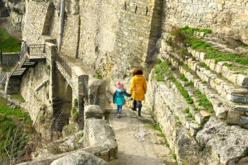 Little girl with mother walking on the slope along the giant medieval stone wall near fortress of Kamianets-Podilskyi, Ukraine