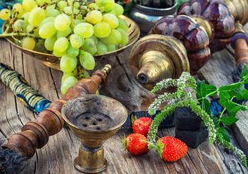 Old smoking  hookah and bunch of grapes on wooden surface.