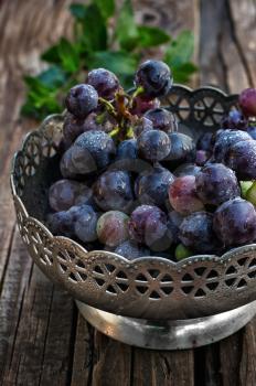 Brush ripe and juicy grapes in  vintage iron vase on wooden background