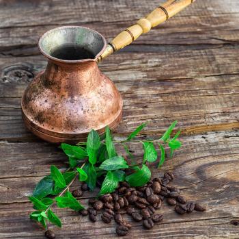 Vintage copper Turk on wooden background covered coffee beans with mint petals.