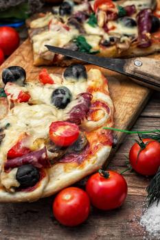 hunk of delicious meat pizza with bacon and olives on the background of the vegetables.The image is tinted