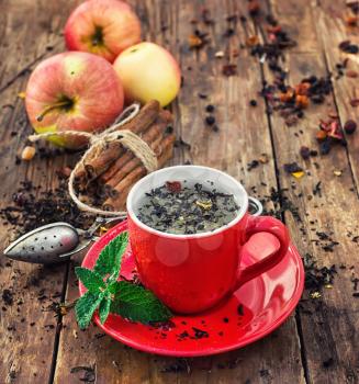 Cup of brewed herbal tea on wooden background strewn with tea leaves