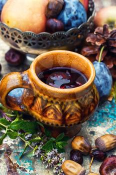 Mug with herbal medicinal tea on an autumn fruit,chestnuts and acorns on metal background.