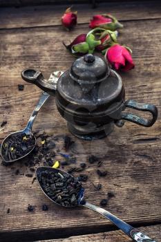 Dried tea leaves in spoons on stylish background of the teapot.