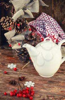 Porcelain pot and decorative wicker wreath with cones on wooden background