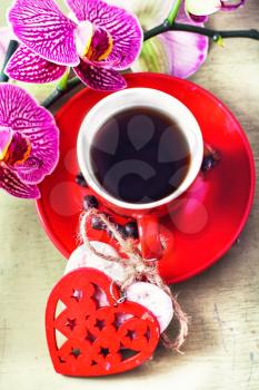 Red Cup decorated with symbolic hearts with black coffee and a flowering branch of orchids