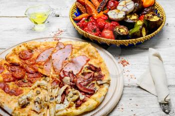 Pizza with meat and bacon and dish of roasted vegetables