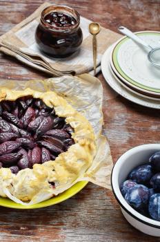 Rustic pie with plums and plum jam on wooden background