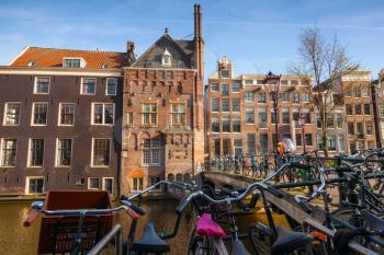AMSTERDAM, NETHERLANDS - MARCH 19, 2014: Colorful houses on the canal coast in spring sunny day. Bicycles stand parked on the bridge 