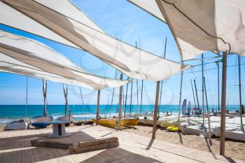 Awnings in sails shape covering relax area near sailing boats on the sandy beach in Calafell town, coast of Mediterranean sea, Catalonia, Spain