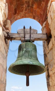 Ancient bell hanging in stone arch, fortress of Calafell town, Spain