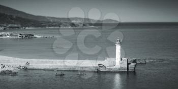 White lighthouse tower on the pier. Entrance to Propriano port, Corsica, France. Monochrome photo with shallow focus effect