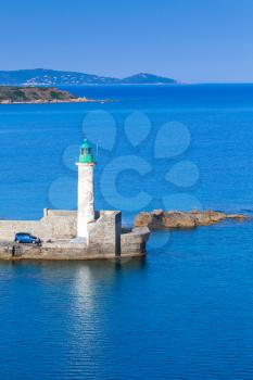 Old lighthouse on the pier, entrance to Propriano port, Corsica, France. White round tower made of stone with green top