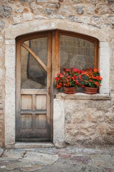 Old wooden door with red flowers on the windowsill. Kotor town, Montenegro