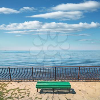 Empty green wooden bench stands on the sea coast in summer day