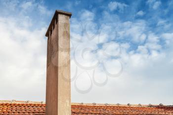 Tall chimney on red tile roof with cloudy sky background