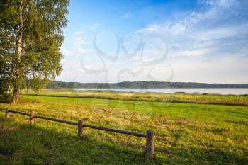 Old wooden fence  and trees on the lake coast, Russian landscape