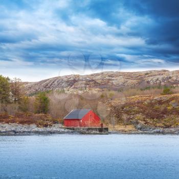 Traditional Norwegian red wooden boat barn with crane on the seacoast