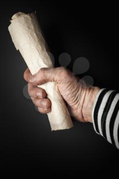 Strong sailor hand holds rolled old crumpled paper sheet over black background, pirate map  concept. Vertical photo