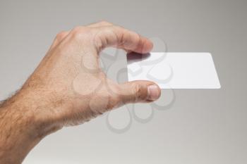 Male hand with white empty card on gray wall background, closeup studio photo with selective focus