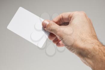Male hand with white empty card over gray wall background, close-up photo with selective focus