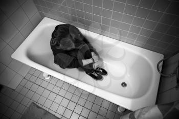 Stressed sad Caucasian teenage girl sitting in empty bath. Black and white photo. Depression concept