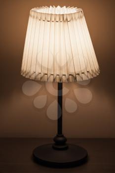 Classical lamp with round fabric lampshade stands near the wall in dark room