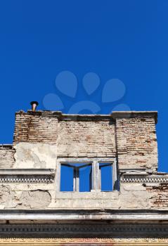 Collapsing facade of an old house with empty windows under blue sky