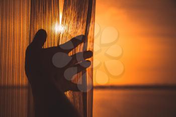 Male hand opens tulle on window with bright orange sunlight outside