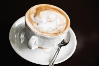 Cup of cappuccino. White mug of coffee with milk foam over black table background, selective focus