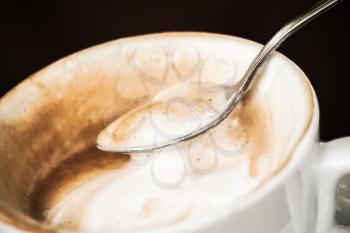 Cappuccino coffee. Milk foam in spoon over black background