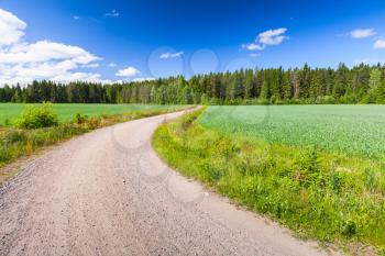 Turning empty rural road under blue sky with clouds in bright summer day. Empty landscape background photo of Finland