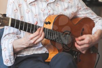 Live music background. Man plays vintage acoustic guitar, close-up photo with selective focus on hands 