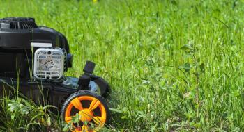 Lawn mower or grass cutter stands on fresh green lawn, closeup photo, side view