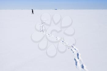 Footsteps of lonely person walking along the endless snowfield 