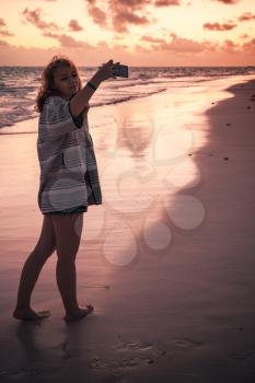 Teenage girl taking selfie photo on the beach in early morning
