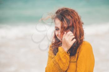 Outdoor portrait of pretty Caucasian teenage girl with red hair on the ocean coast, vintage tonal correction filter effect