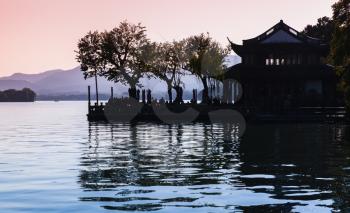 Black trees silhouette and traditional Chinese buildings on the coast of West Lake. Famous public park in Hangzhou city, China