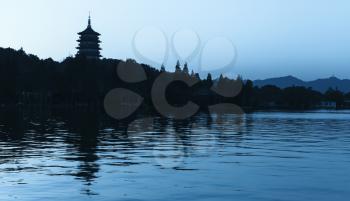 Black silhouette of traditional Chinese pagoda on blue evening sky background. Coast of West Lake. Famous public park of Hangzhou city, China