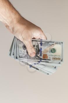 Vertical photo. Fan of One Hundred Dollars notes in male hand over gray wall background