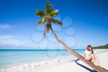 Young girl sitting on a palm tree. Saona island beach. Atlantic ocean coast, Dominican Republic