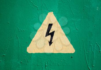 Yellow high voltage triangle warning sign on green metal wall