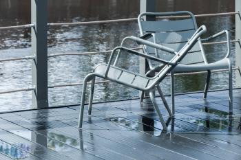 Two outdoor gray metal chairs stand on wet pier