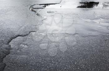 Street asphalt in bad condition, puddle and cracks on urban pavement