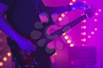 Live rock music background, guitarist tunes electric bass guitar, close-up photo with soft selective focus and purple illumination