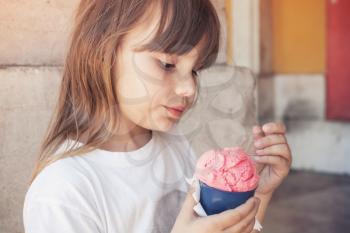 Little blond European girl eats pink fruit ice cream, close-up outdoor portrait 
