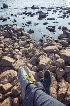 Male and female feet in sporty shoes lay on coastal rough stones. Family travel lifestyle, vertical photo