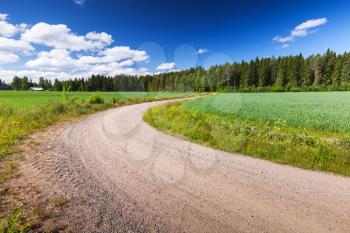 Turning rural road goes near green field under blue sky in summer day. Empty landscape background, Finland