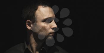 Close-up profile portrait of young European man over black background, low key studio photo