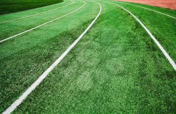 Empty running track with bright green artificial turf and white lines